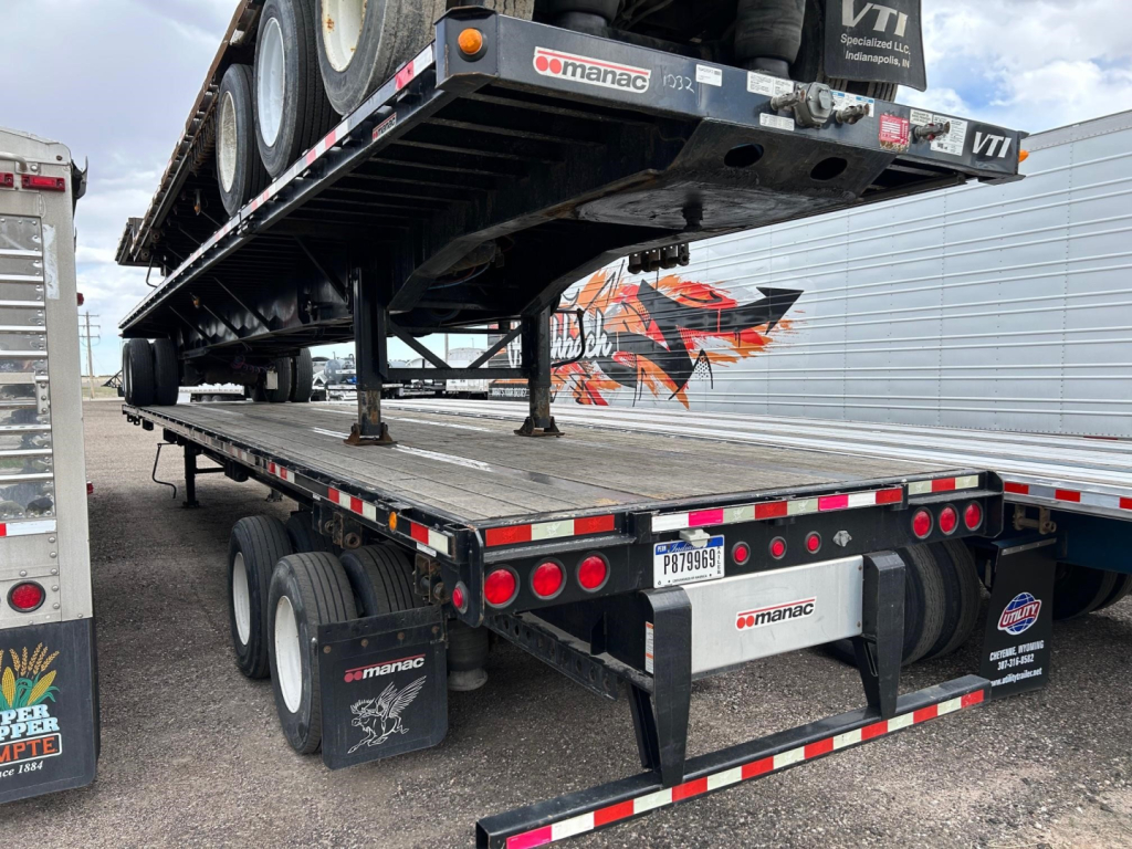 Manac flatbed trailer with extendable steel deck showing rear and undercarriage details including red taillights and mud flaps.