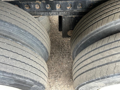 Trailer axles and dual tires seen from above between the wheels of a 2019 Manac extendable steel flatbed trailer, close-up view of tires and frame.