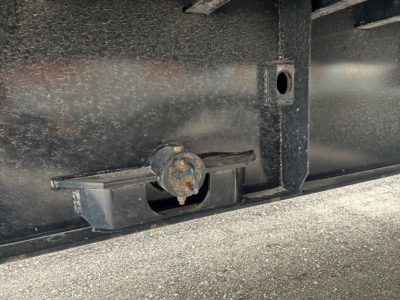 Trailer hitch latch on the underside of a Manac extendable flatbed trailer showing a circular latch mechanism and surrounding metal structure.