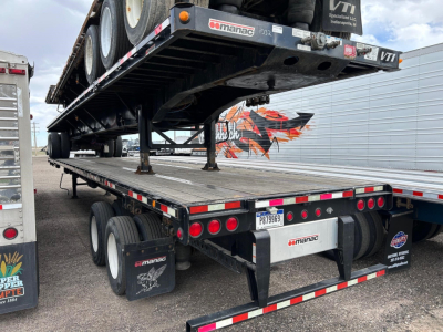 Manac flatbed trailer with extendable steel deck showing rear and undercarriage details including red taillights and mud flaps.