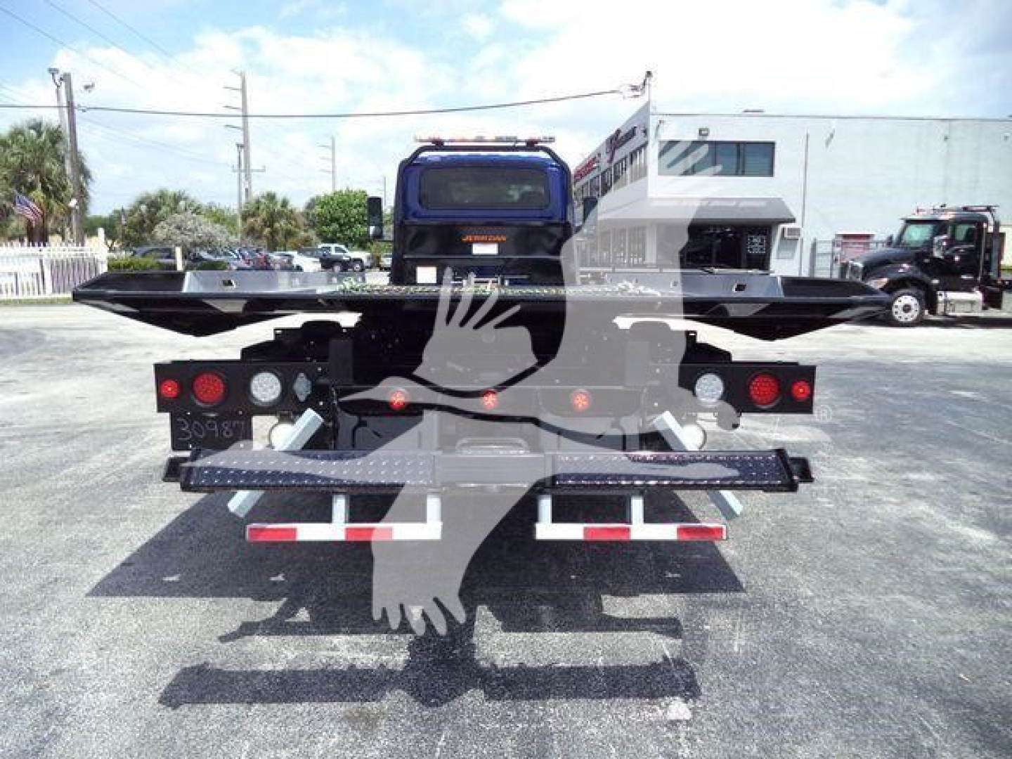 Rear view of a 2027 International MV rollback truck showing flatbed and taillights, with stock number MV607EXCABBLU visible in a dealership lot