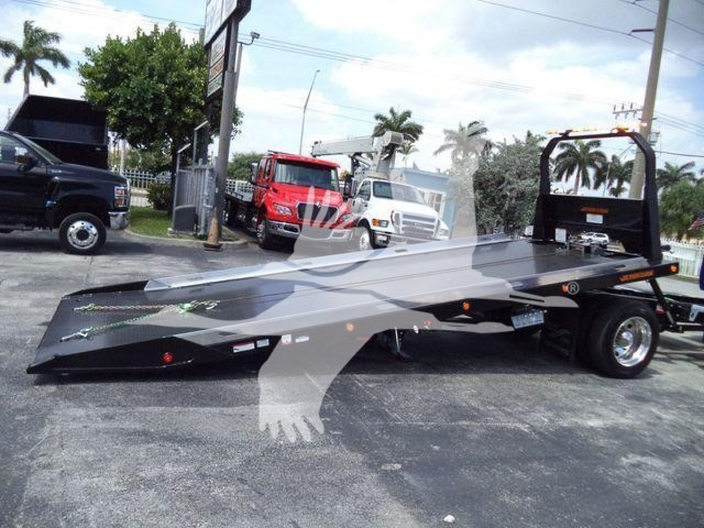 Truck rollback tow bed trailer showing a lowered flatbed with a black finish and a gooseneck hitch from a side view.
