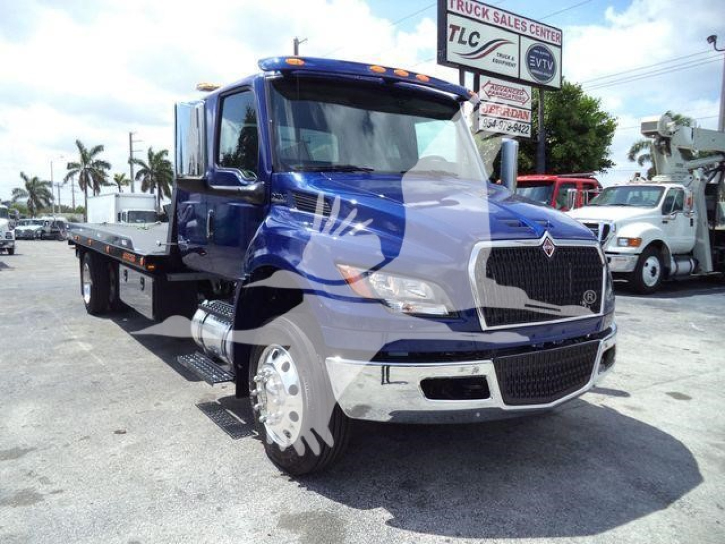 Blue 2027 International MV rollback truck showing front grille and flatbed seen in a dealership lot.