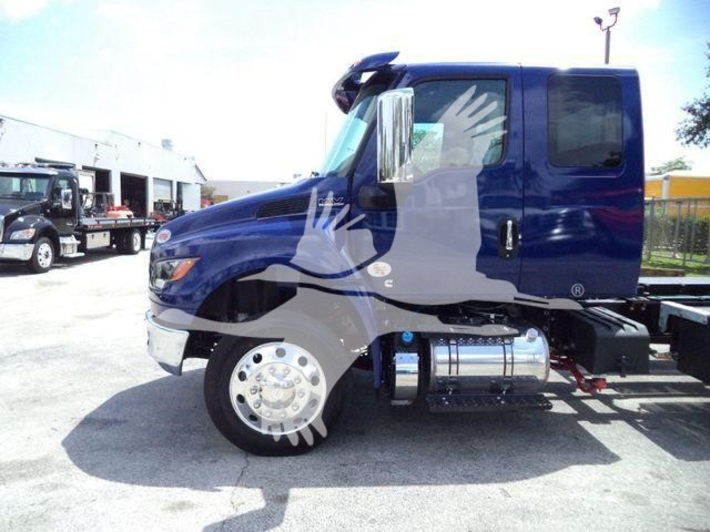 Truck cab side view showing blue International MV truck with chrome dual fuel tanks and large wheel, rollback category, stock MV607EXCABBLU.