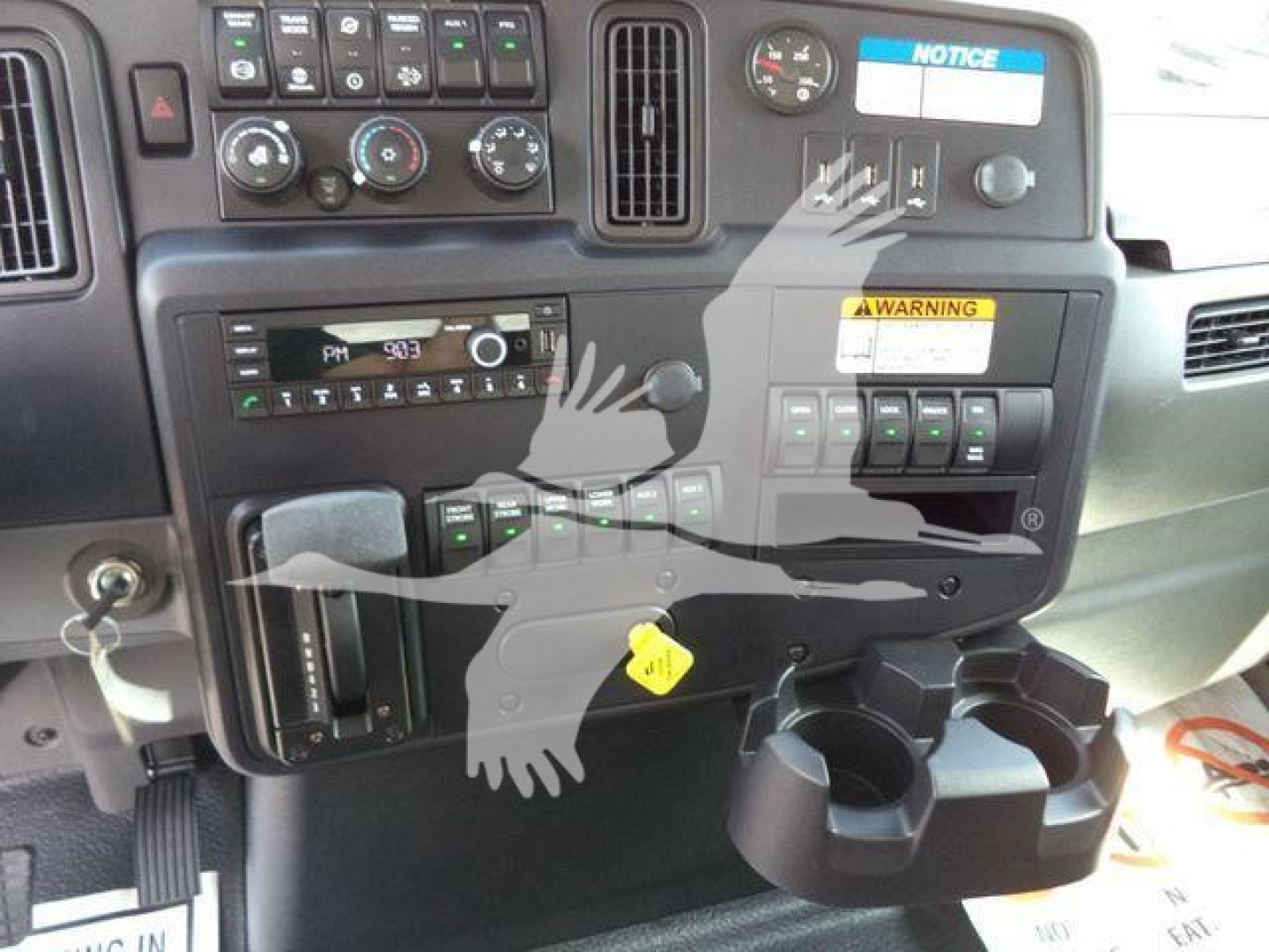 Dashboard of a 2027 International MV truck showing instrument cluster, climate controls, radio, warning labels, and cup holders.