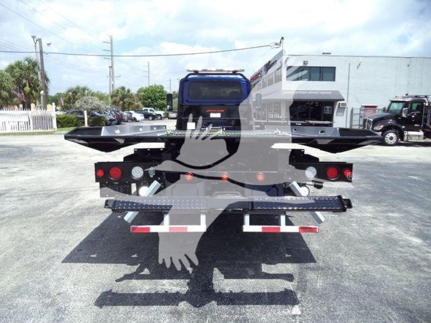 Truck flatbed rear view showing safety lights and reflective tape; tail lights and hydraulic components visible.