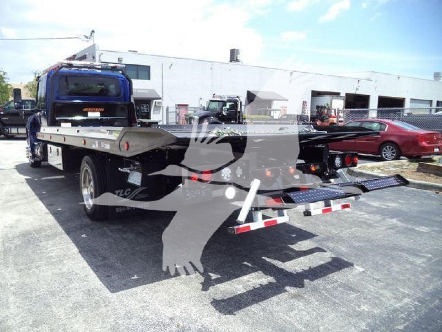 Flatbed tow truck in a dealership lot showing rear view with dual ramps and blue cab; MV607EXCABBLU stock visible in listing.