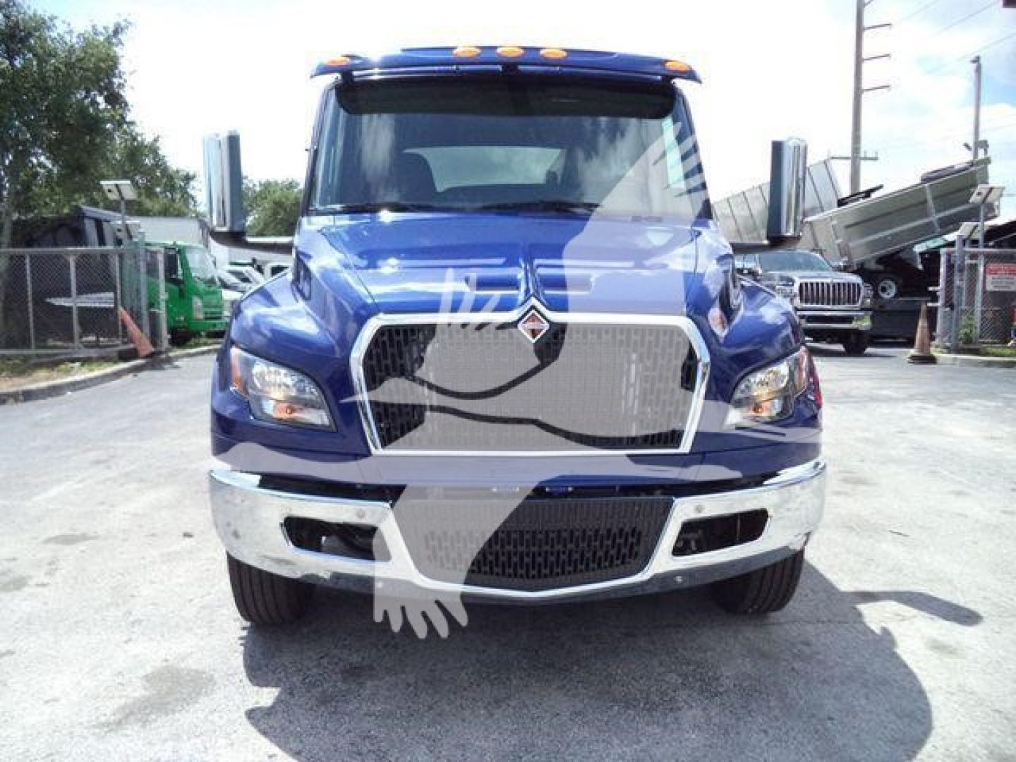 Truck front view showing blue cab with large chrome grille, International logo, and bumper; rollover hitch area and headlights visible.