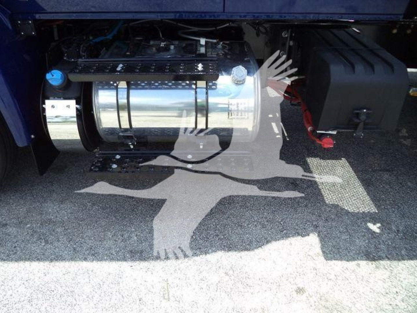 Truck undercarriage showing chrome fuel tank and battery box with hoses; limited view of chassis and ground shadow.
