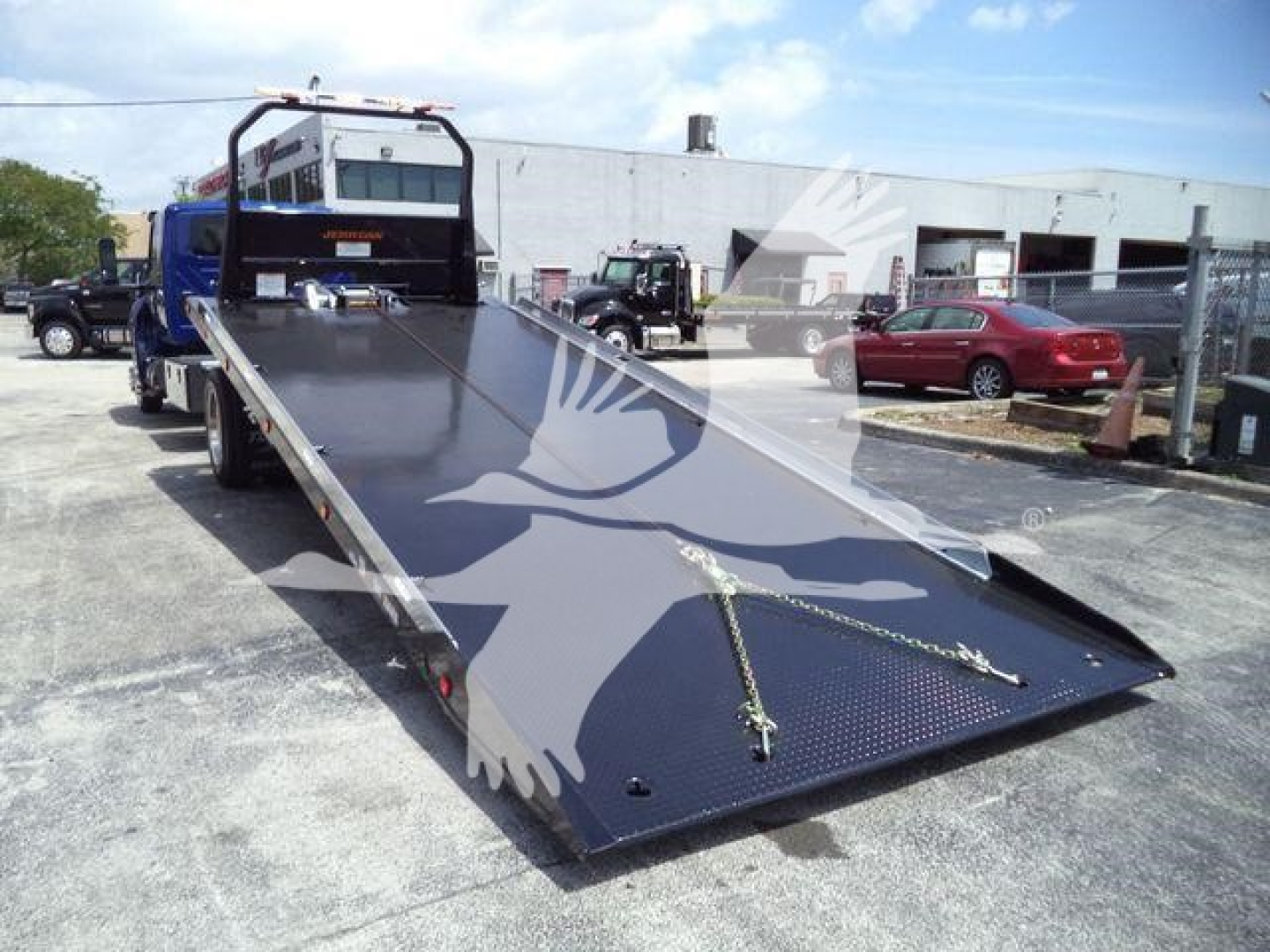 Truck tilt-bed on a rollback tow truck with a blue cab and open ramp, loading area in view.
