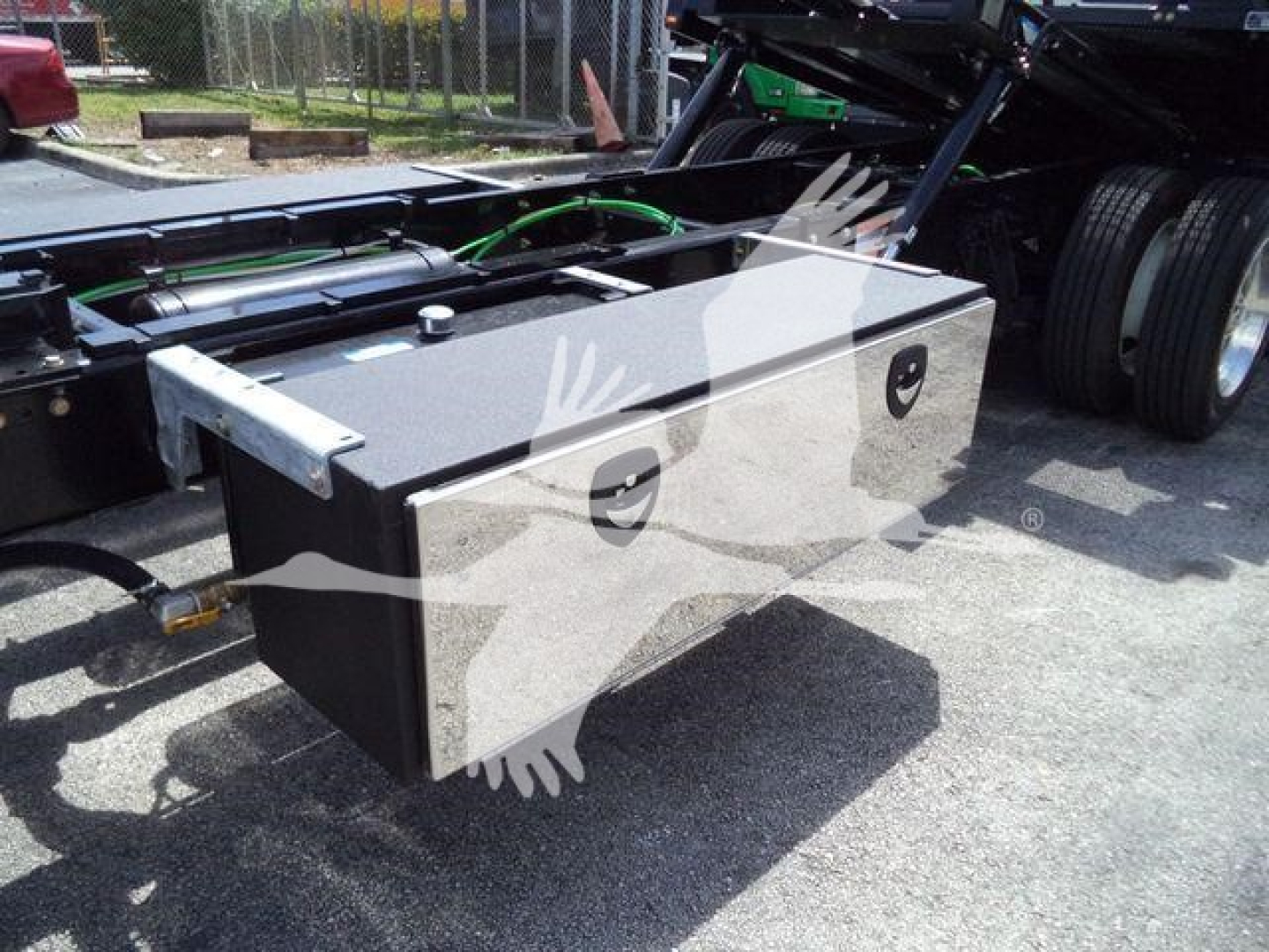 Truck chassis with a large rectangular aluminum toolbox mounted behind the cab, visible fuel lines and chassis components nearby, International MV cabover/tractor area