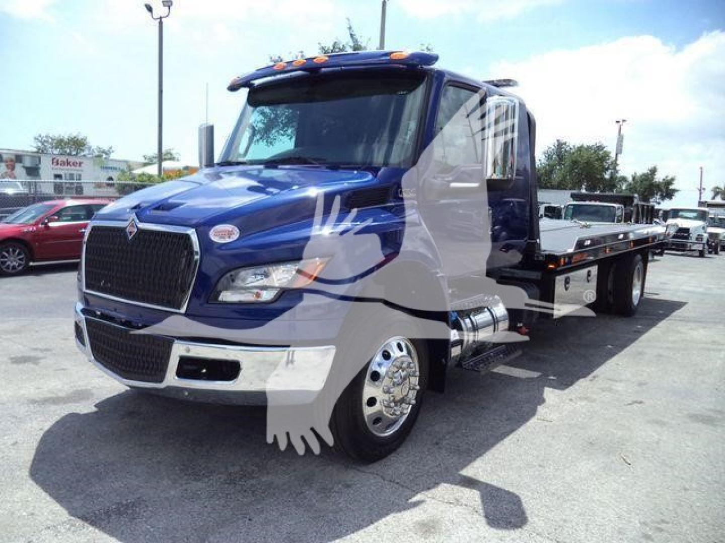 Truck in blue color with flatbed, International MV model, front grille, header and wheel, side mirrors, and rollback bed visible.