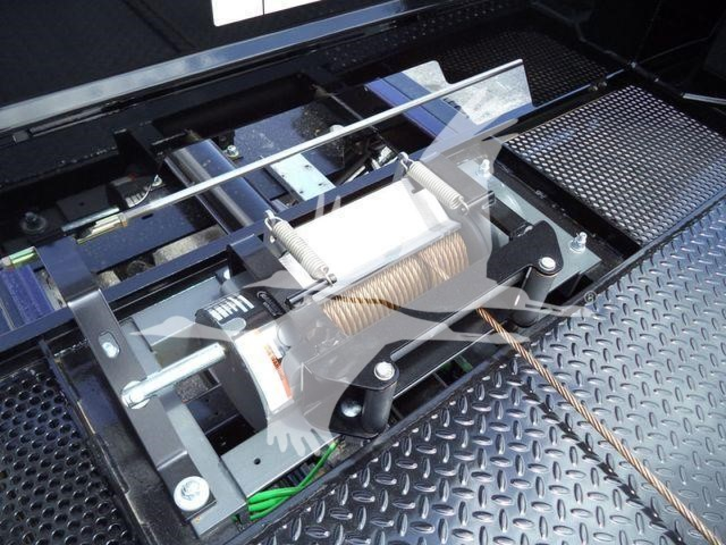 Winch mechanism and steel rollers under a truck bed, with visible cables and metal framework.