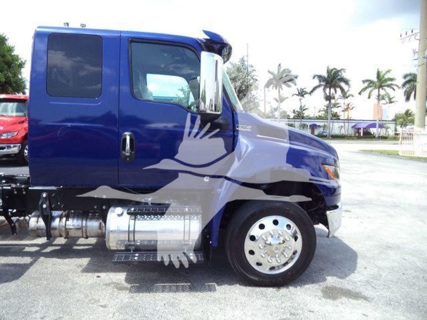 Side view of a blue 2027 International MV truck cab with chrome fuel tanks and steps, showing side door, wheel, and part of front fender.