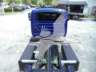 Blue truck cab of a 2027 International MV with a flatbed chassis and exposed green-wired components between the cab and the chassis.