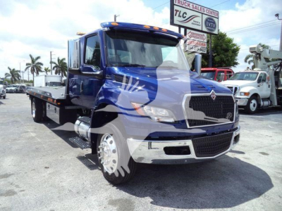 Blue 2027 International MV rollback truck showing front grille and flatbed seen in a dealership lot.