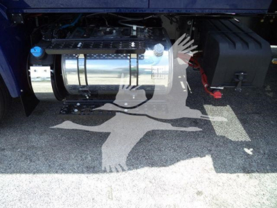 Truck undercarriage showing chrome fuel tank and battery box with hoses; limited view of chassis and ground shadow.