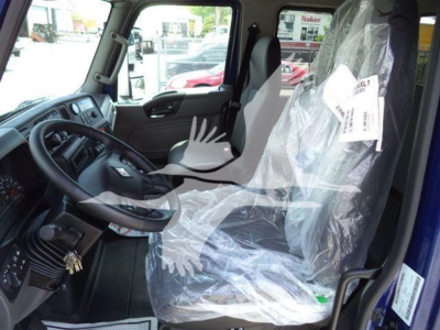 Truck interior with plastic-covered driver seat and dashboard view, steering wheel and pedals visible; new truck cab in factory plastic.