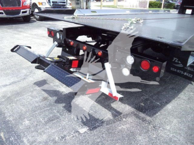 Rear view of a flatbed tow truck showing hydraulic wheel lift and safety steps, with taillights and bumper hardware visible.