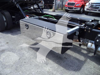 Truck frame with a large metallic toolbox mounted; visible are the toolbox lid, side handle, and chassis components; background shows other trucks.