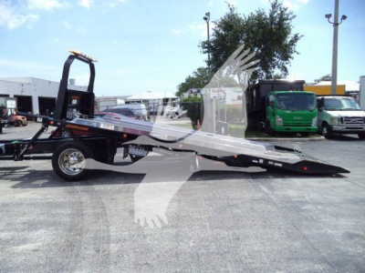 Tow truck with a low-profile car carrier bed extended, black color with orange accents, side branding, hydraulic ramps, in an industrial lot.