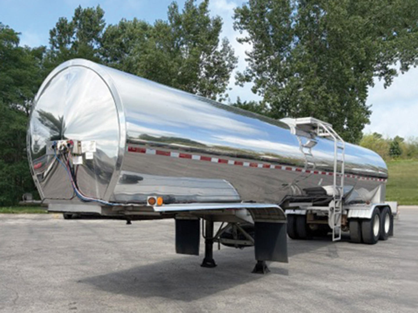 Tank trailer in-service with polished chrome finish showing tandem axles and landing legs and a ladder to access the top hatch.