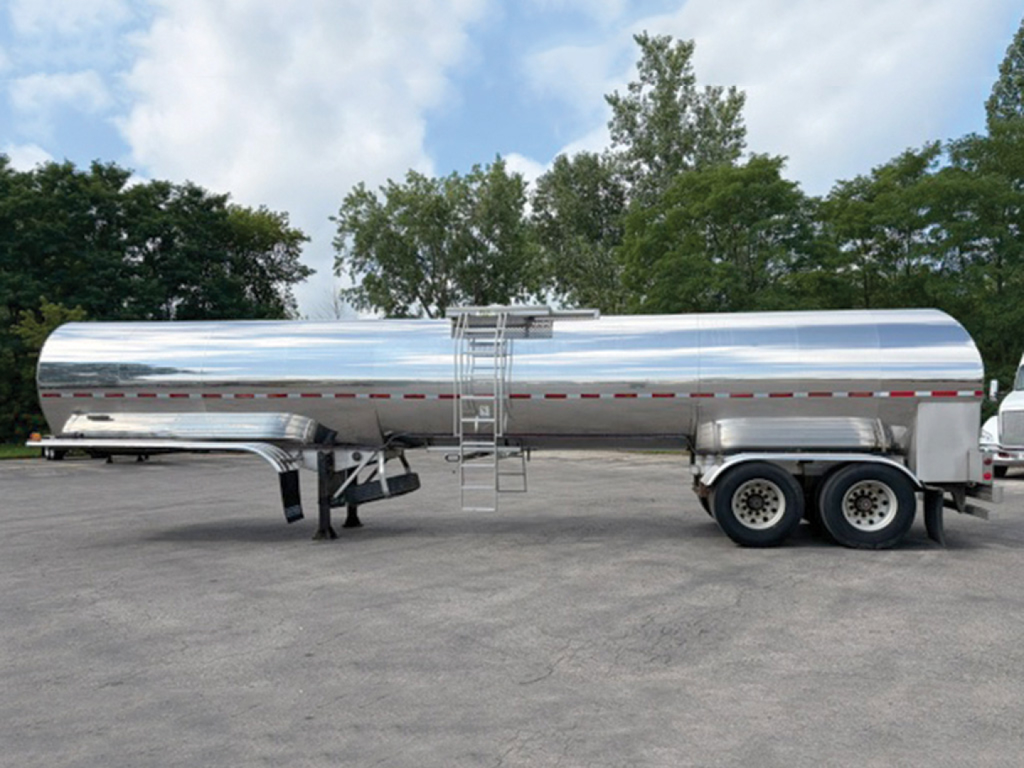 Tank trailer showing polished stainless steel cylindrical tank on dual-axle trailer with ladder and safety rails.