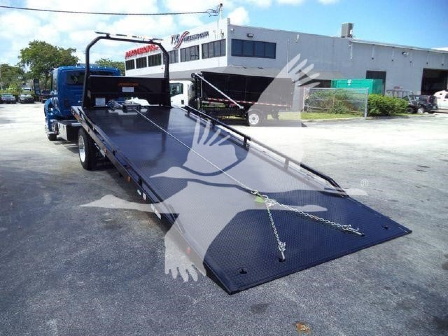 Truck bed with hydraulic rollback trailer in a parking lot, International MV (2027) branding not visible.