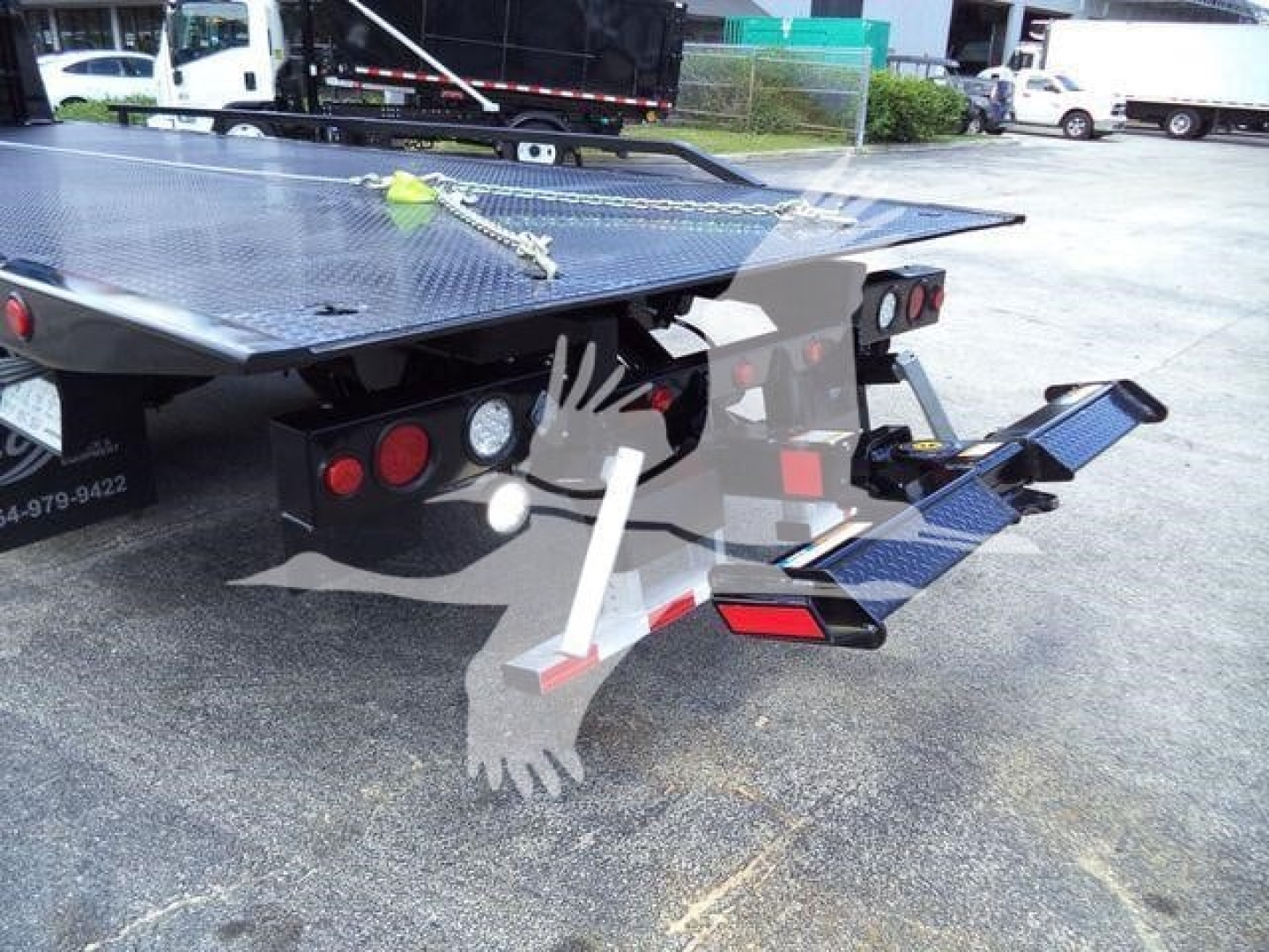 Truck rollback bed rear showing hydraulic components and rear lighting, taillights, and folding ramp with diamond plate surface.