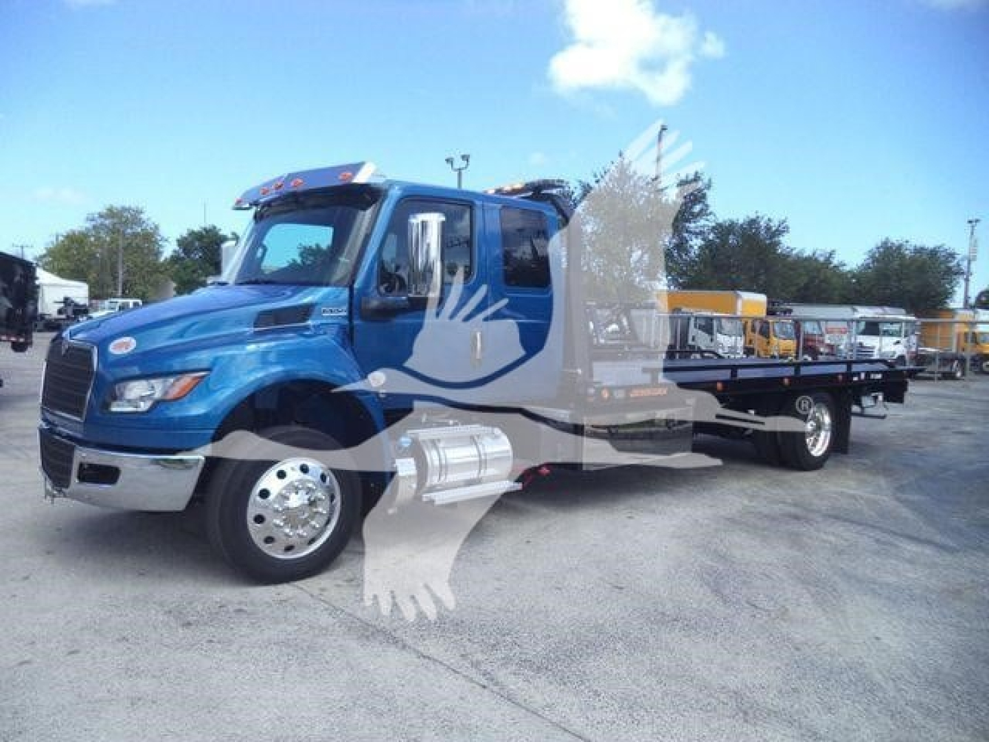 Blue 2027 International MV rollback truck shown in a dealership lot with a side carrier and chrome fuel tanks.