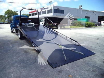 Truck bed with hydraulic rollback trailer in a parking lot, International MV (2027) branding not visible.