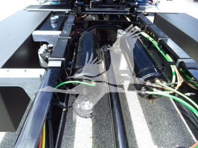 Truck chassis showing hydraulic lines and frame components, with green hoses and electrical wiring visible between rails.