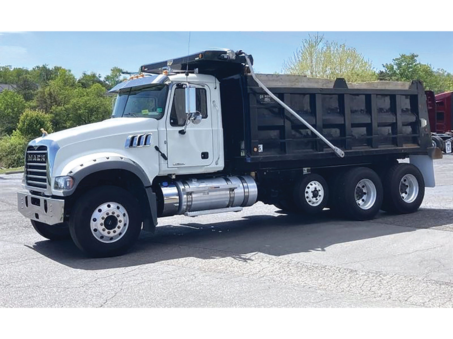 Truck image: 2023 Mack GR 64F dump truck, white cab, black dump bed, three rear axles, chrome fuel tanks, side steps, and hydraulic lines visible.