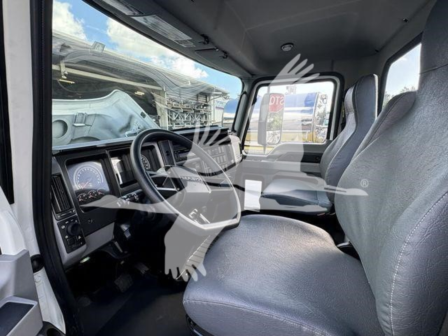 Cab interior of a 2023 Mack MD7 truck showing driver's seat, steering wheel, and dashboard with gauges and a side mirror.