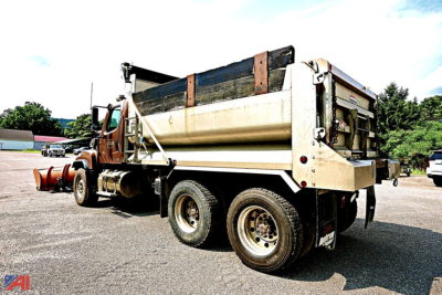 Dump truck side/rear view showing bed in raised position and plow attachment visible at front; 2013 Freightliner SD114 dump truck.