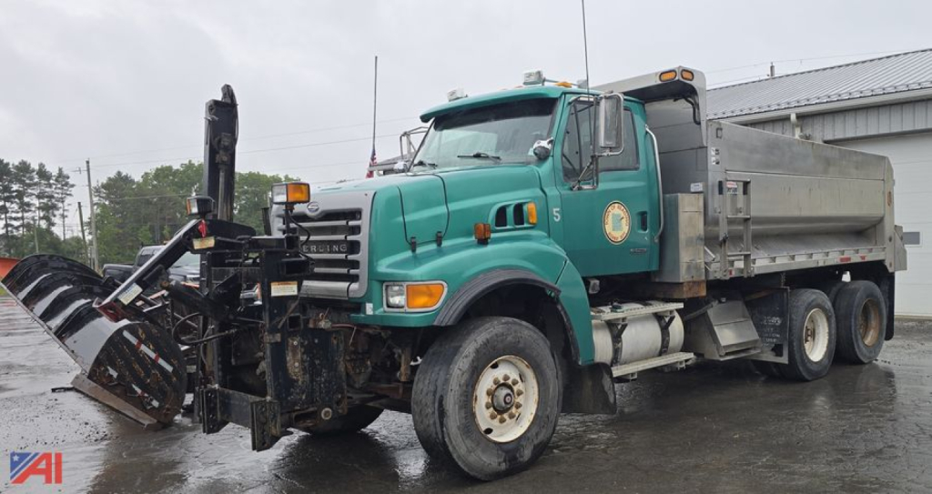 Dump truck in service showing front-mounted snow plow or attachment and green cab with Sterling emblem.
