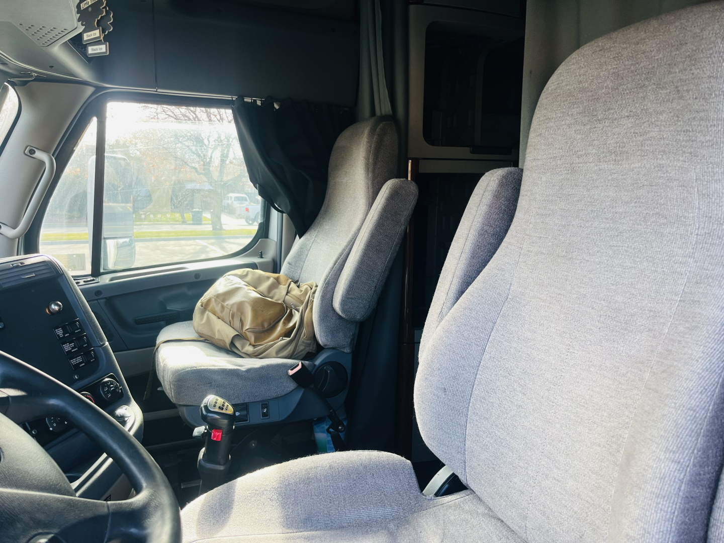Truck cab interior showing driver and passenger seats with gray upholstery and a cluttered area near the dash; Freightliner cascadia 125 used truck interior view