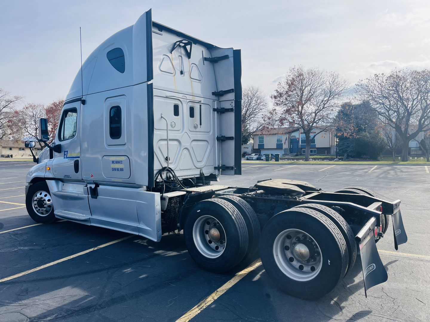 Side view of a 2013 Freightliner Cascadia 125 conventional sleeper tractor in a parking lot, showing rear axles and chassis with visible tires and mud flaps.