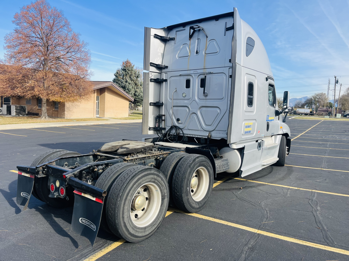Vehicle side/back view of a 2013 Freightliner Cascadia 125 semi-truck tractor in a parking lot showing the rear wheels and fifth wheel area.
