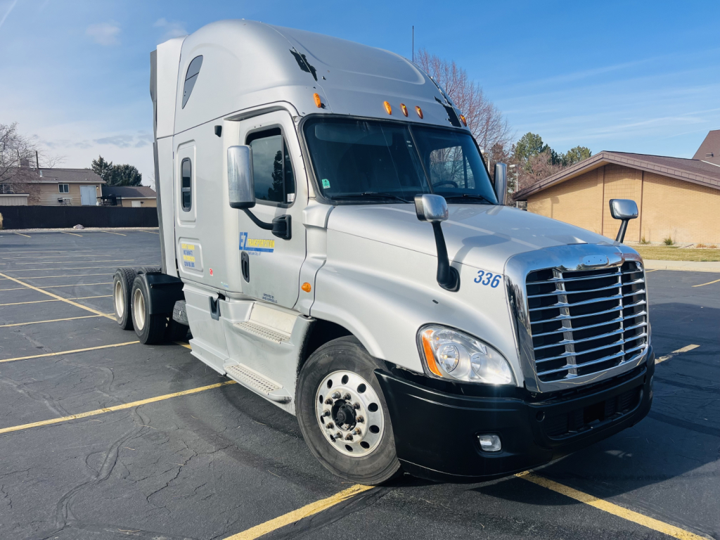 Truck side view showing Freightliner Cascadia 125 cab with sleeper. Front grille, headlamps, and side mirrors visible.