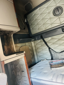 Cab interior of a Freightliner Cascadia 125 showing quilted light gray door panel, storage net, and sleeper area.