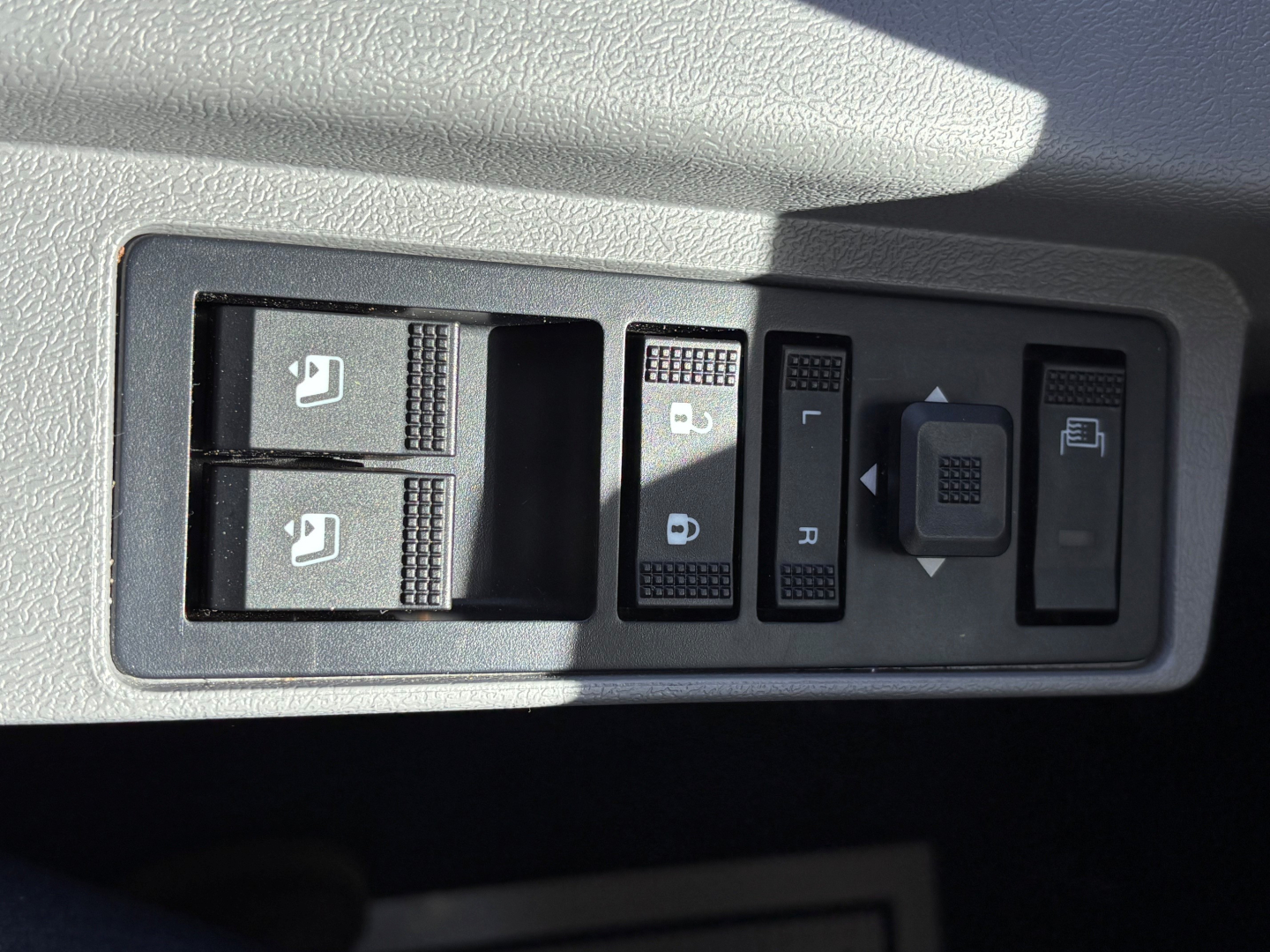 Panel view showing window/lock switches and mirror controls inside a Mack GR64B truck cab. Includes two window switches, central locking, and mirror adjustment controls.
