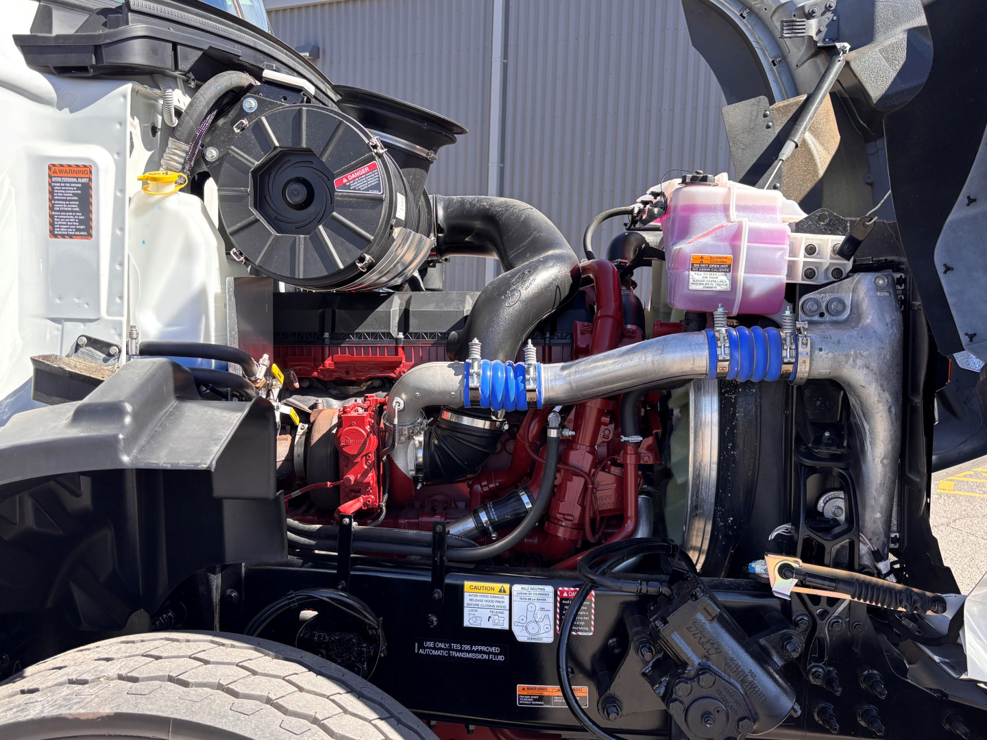 Mack GR64B engine bay with visible cooling system, hoses, and pink coolant reservoir. engine components and belts in view.