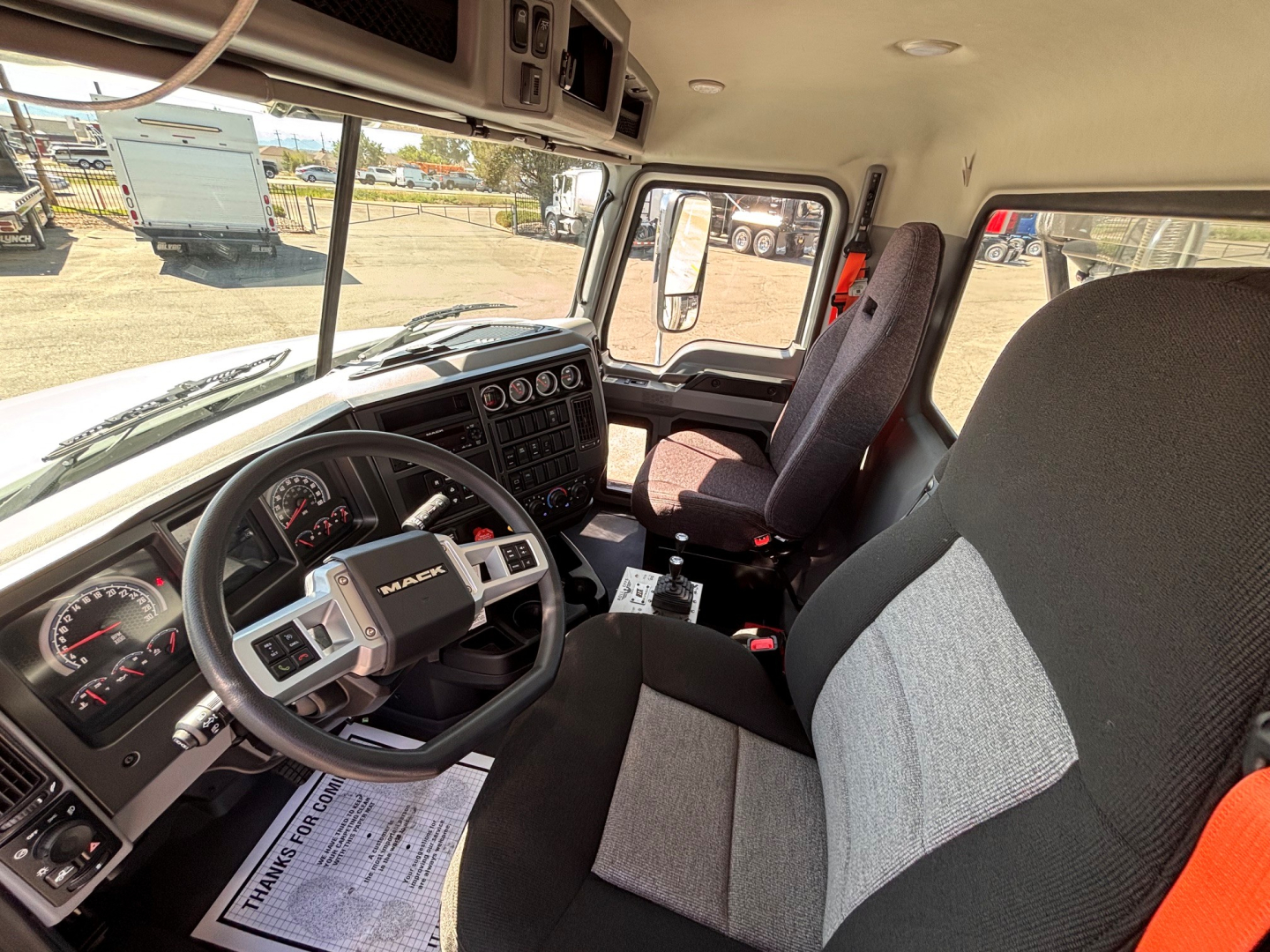 Mack GR64B truck interior showing driver's seat and steering wheel with Dash controls and gauges visible.