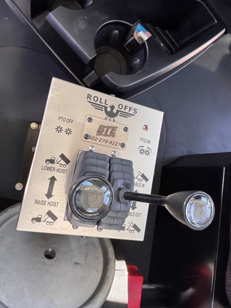 Mack GR64B rolloff control panel showing Roll Offs label, PTO off indicators, lower hoist and raise/lower arrows, and two circular levers with a small keypad area.