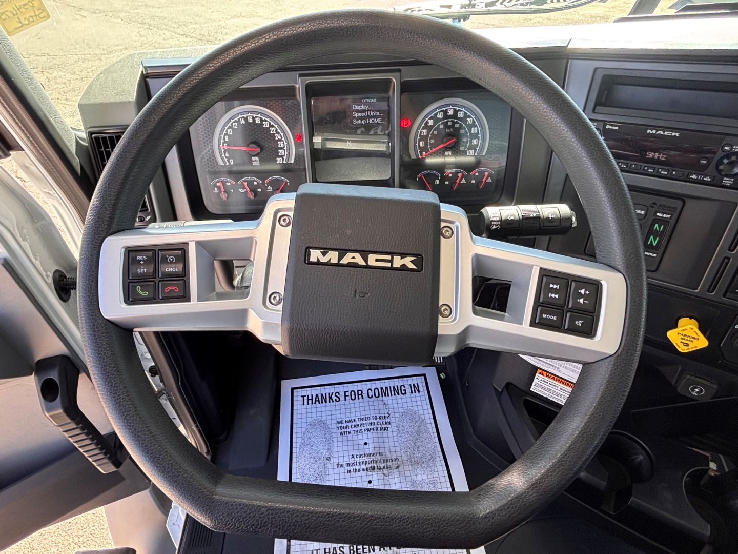 Steering wheel interior of a Mack GR64B truck showing the central Mack badge, instrument cluster, and control buttons on the dashboard.