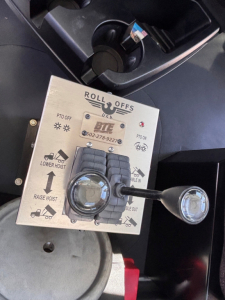 Mack GR64B rolloff control panel showing Roll Offs label, PTO off indicators, lower hoist and raise/lower arrows, and two circular levers with a small keypad area.