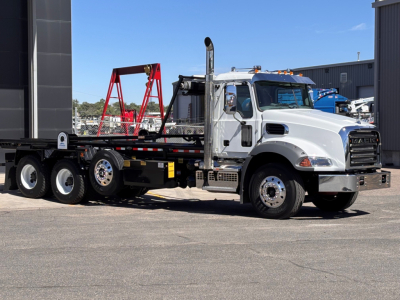 Mack GR64B roll-off truck in showroom setting showing cab with chrome exhaust stack and flatbed, VIN 1M2GR4GC9TM054675, stock 70665.