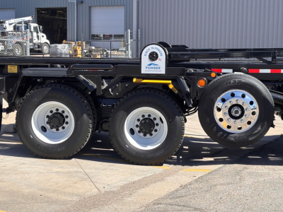 Mack GR64B roll-off truck chassis with triple rear axles and spare wheel showing 10-hole aluminum wheel rims.