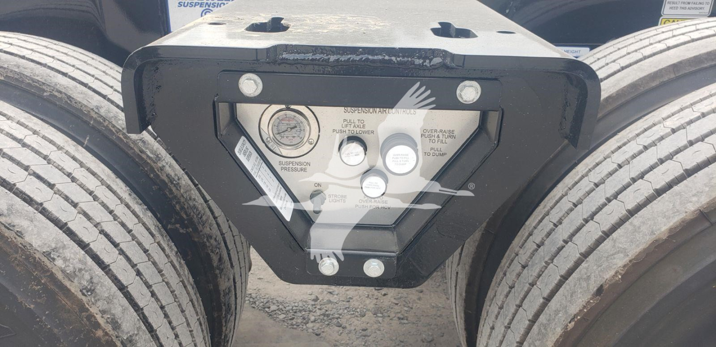Trailer kingpin plate with warning labels and gauges between dual rear axles of a Fontaine Magnitude 55Mx lowboy trailer.